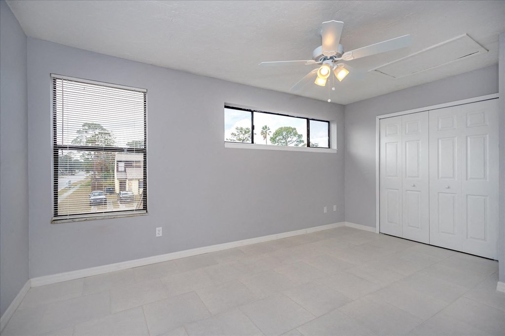 A room with a ceiling fan and two windows.