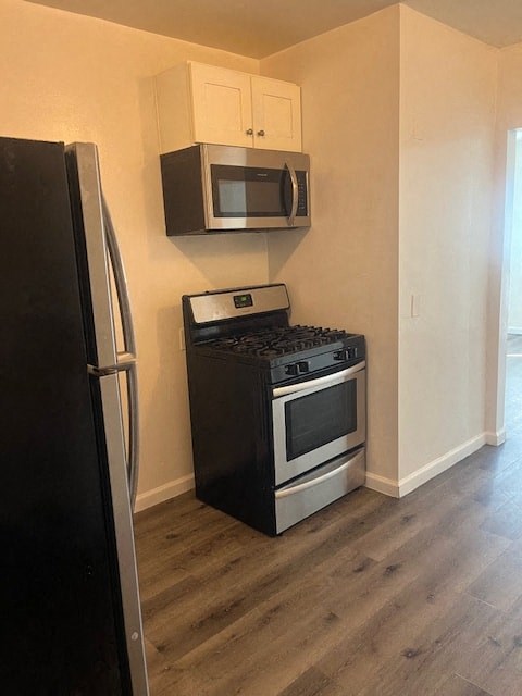 A black refrigerator is in the corner of a kitchen with a black stove and microwave above it.