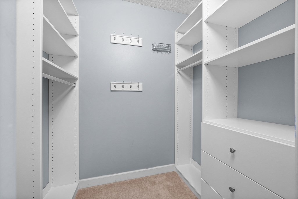 a walk in closet with white shelves and a gray wall
