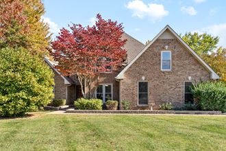 the front of a brick house with a lawn and trees