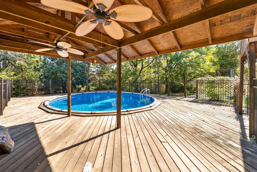 a backyard with a pool and a deck with a ceiling fan