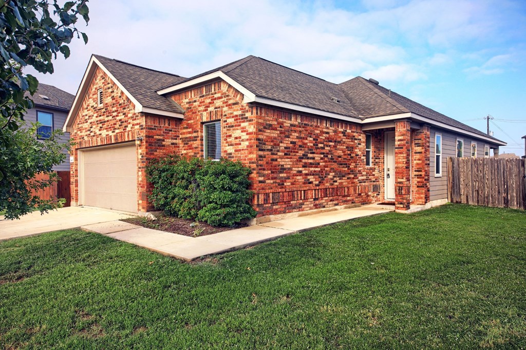 a small brick house with a lawn and a wooden fence