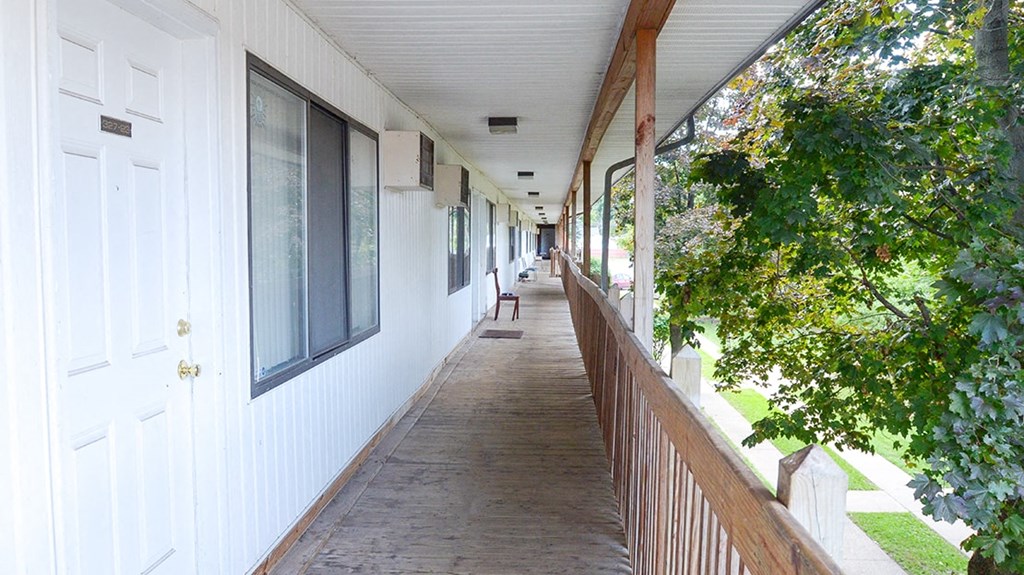 a long porch outside of a white building with trees