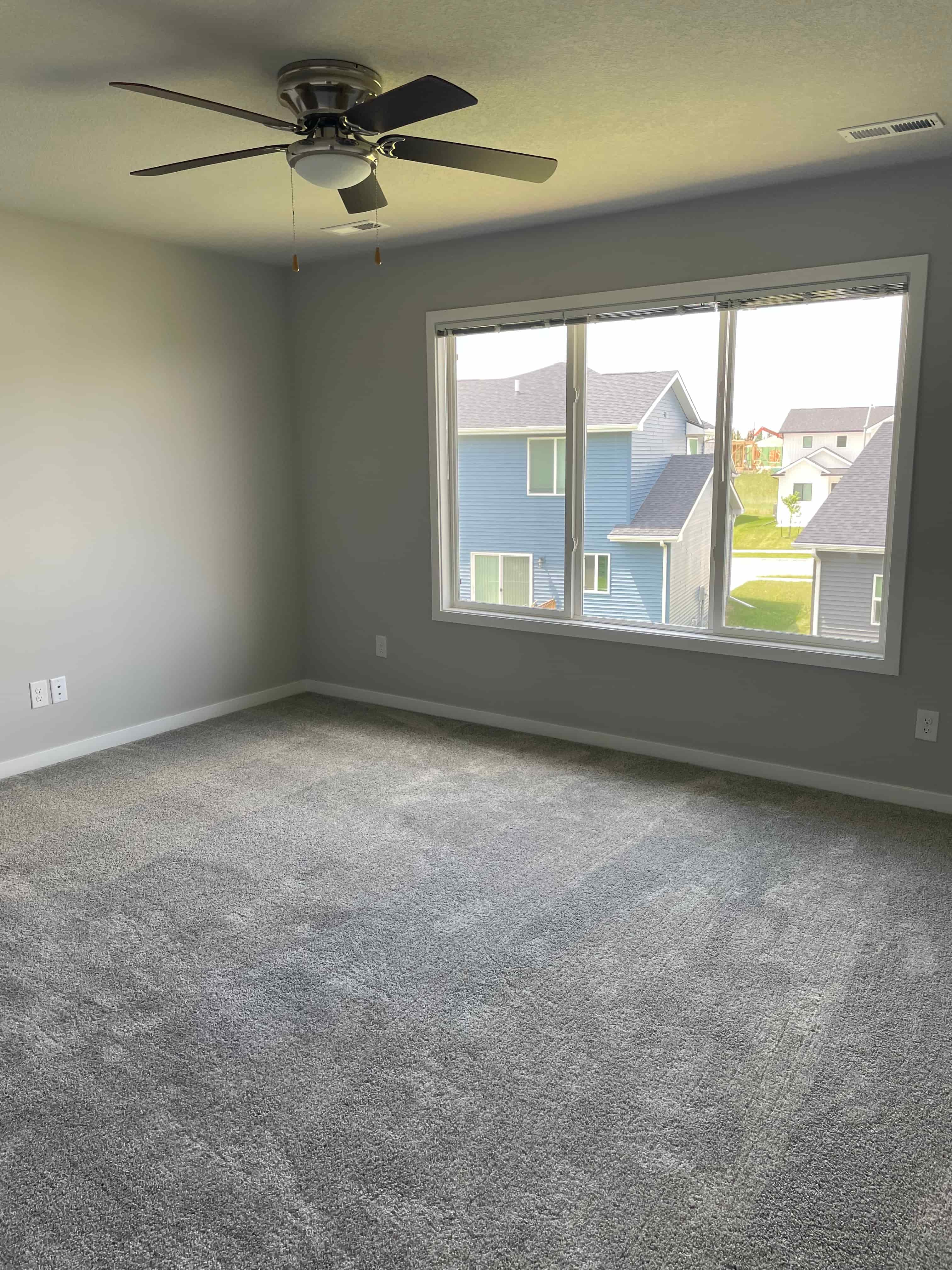 an empty living room with a ceiling fan and a large window