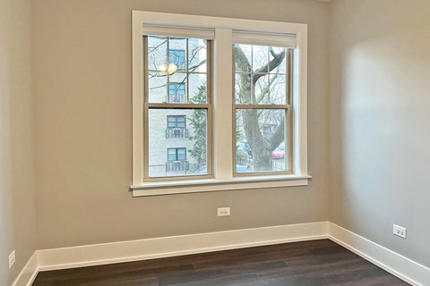 A room with a large window showing a view of a building and a tree outside.