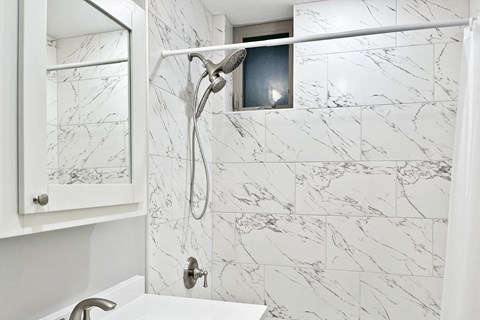 A white bathroom with a marble tile wall and a shower head.