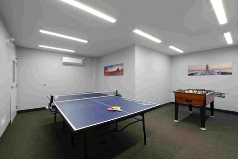 A ping pong table is in the middle of a room with a pool table on the other side.