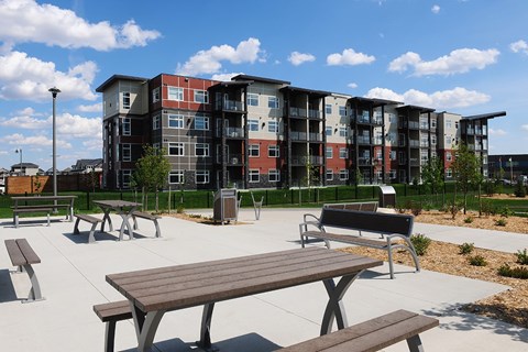 A park with benches and a picnic table in front of apartment buildings.