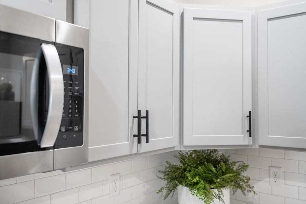 a kitchen with white cabinets and a microwave and a plant