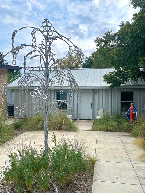 A metal tree sculpture is in the foreground of a building with a grey roof.