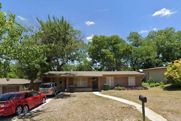 A red car is parked in a driveway in front of a house.