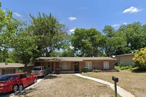 A red car is parked in a driveway in front of a house.