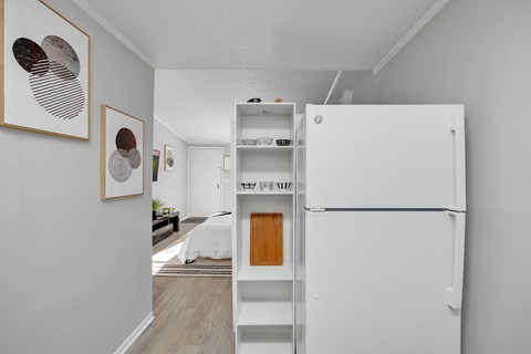 A white refrigerator is in a room with a bed in the background.
