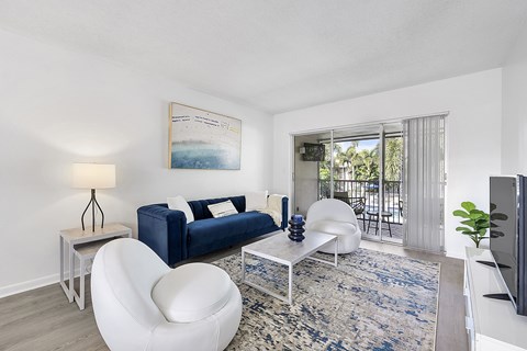 A living room with a blue couch, white chair, and a painting on the wall.