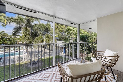 A balcony with a chair and a cushion overlooking a pool and trees.