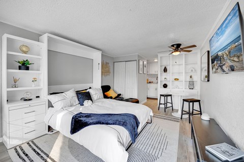 A bedroom with a bed, a ceiling fan, and a painting on the wall.