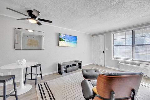 A living room with a ceiling fan, a white table, a black chair, and a painting on the wall.