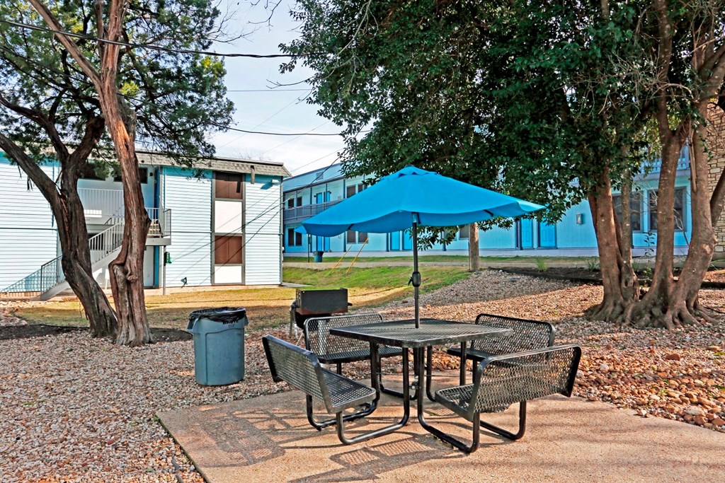 a picnic table with an umbrella and chairs in a park