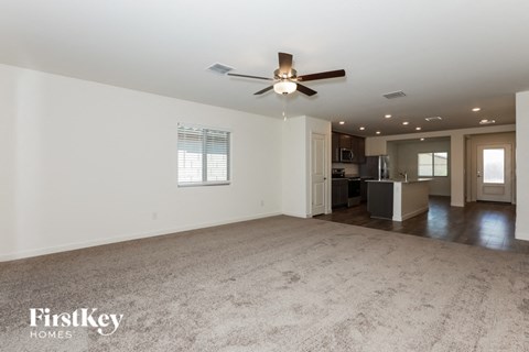 an empty living room with a ceiling fan and a kitchen