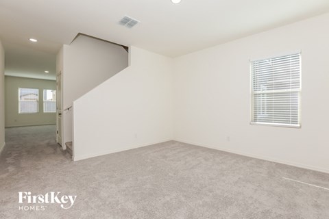 a living room with white walls and carpet and a door to a hallway
