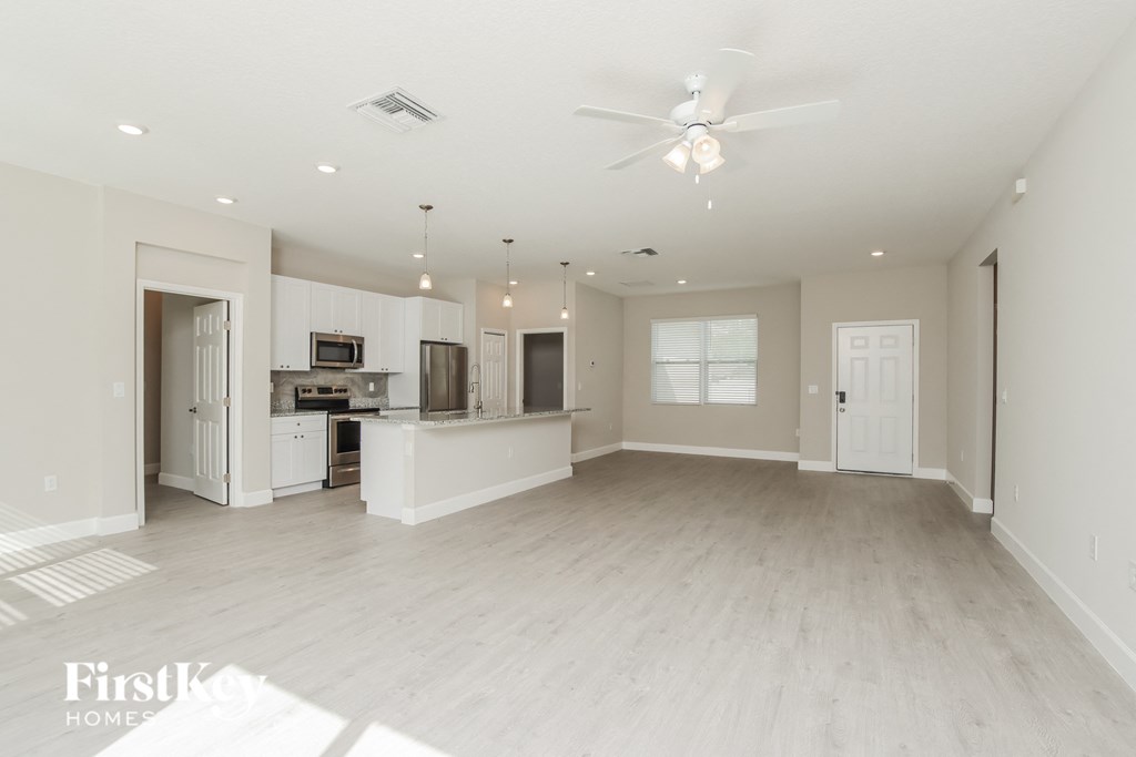 an empty living room with a kitchen and a ceiling fan
