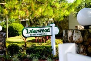 A sign that says Lakewood is in front of a green hedge.