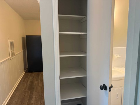 A kitchen pantry with a black refrigerator and white shelves.