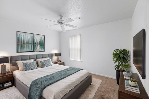A bedroom with a bed, a ceiling fan, and a painting on the wall.