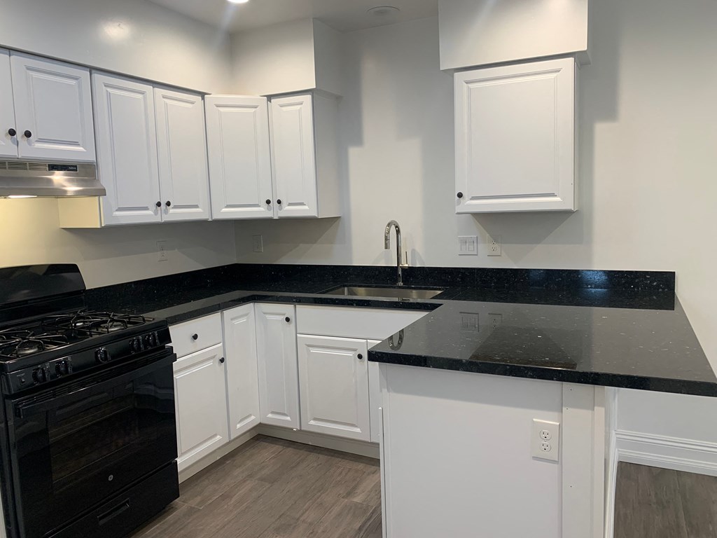 A kitchen with white cabinets and black countertops.