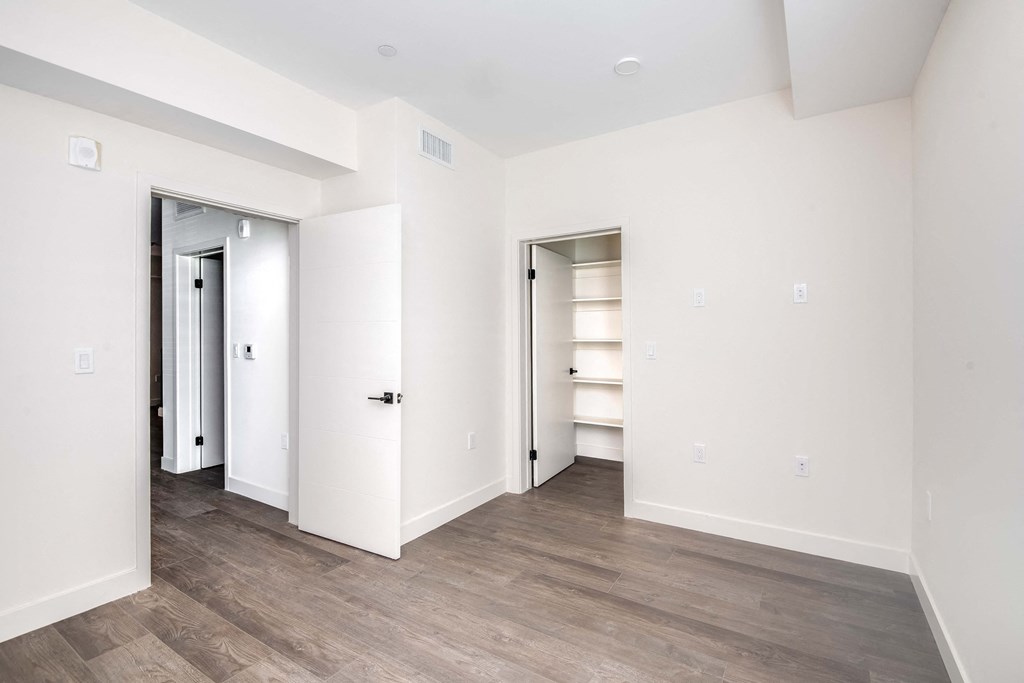 a bedroom with white walls and a closet and wood flooring