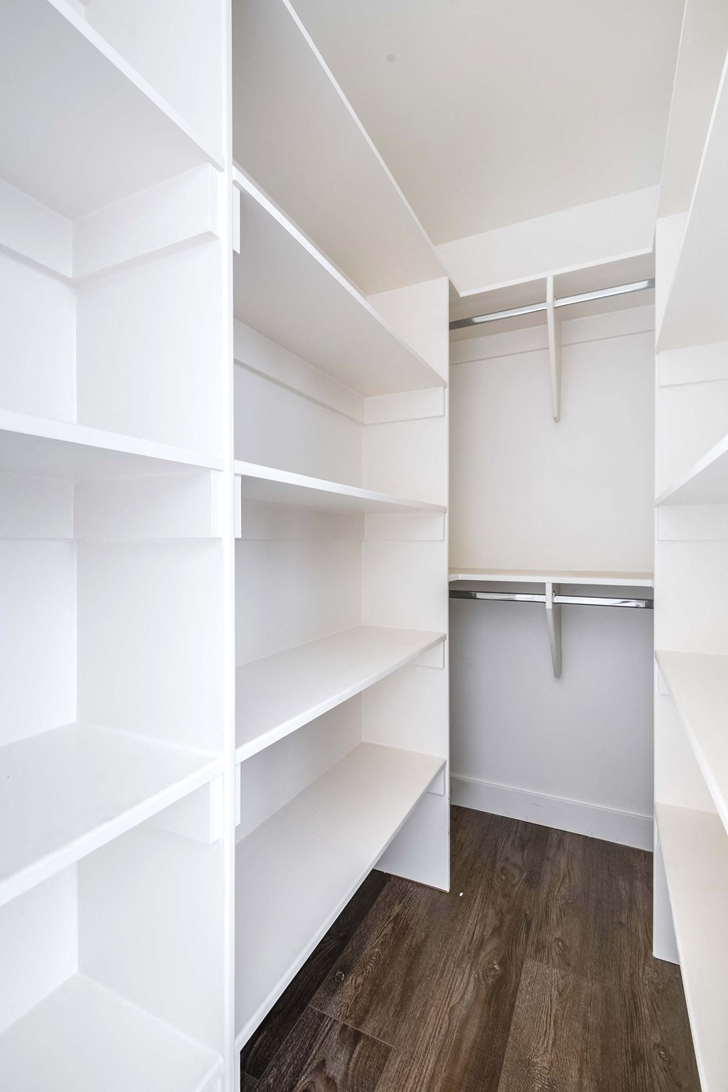 a walk in closet with white shelves and a wood floor