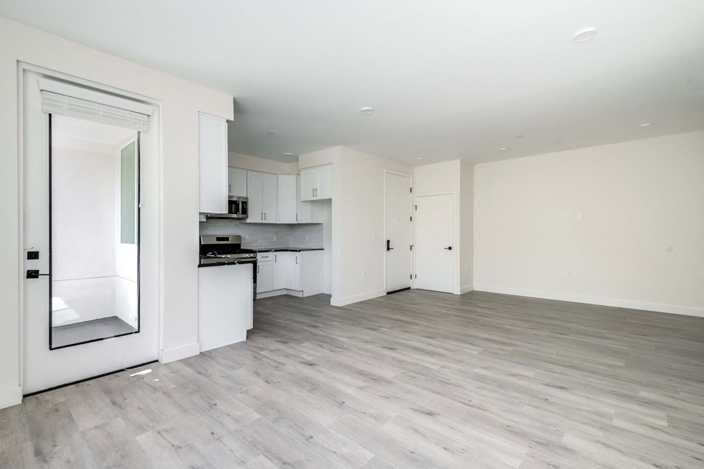 an empty living room and kitchen with white walls and wood flooring