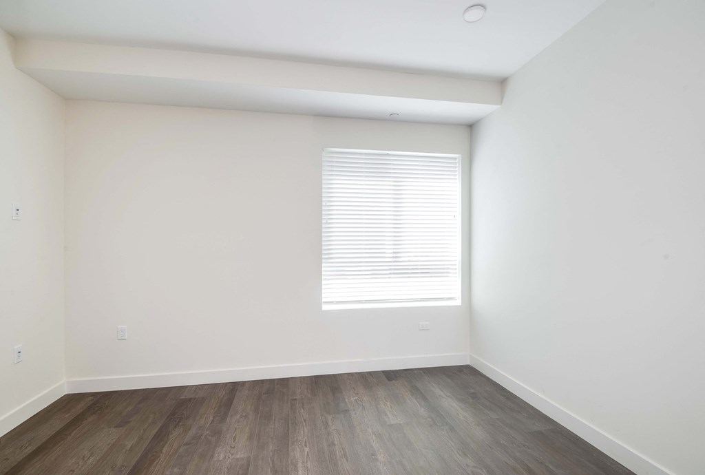 an empty room with white walls and wood floors and a window