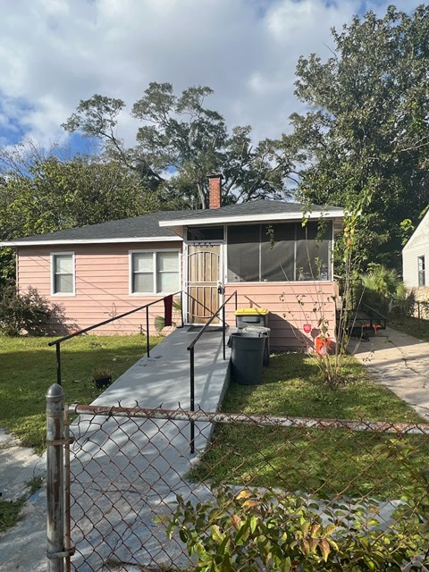 a small pink house with a porch and a chain link fence
