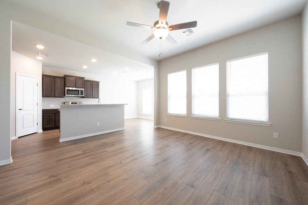 an empty living room with a ceiling fan and a kitchen