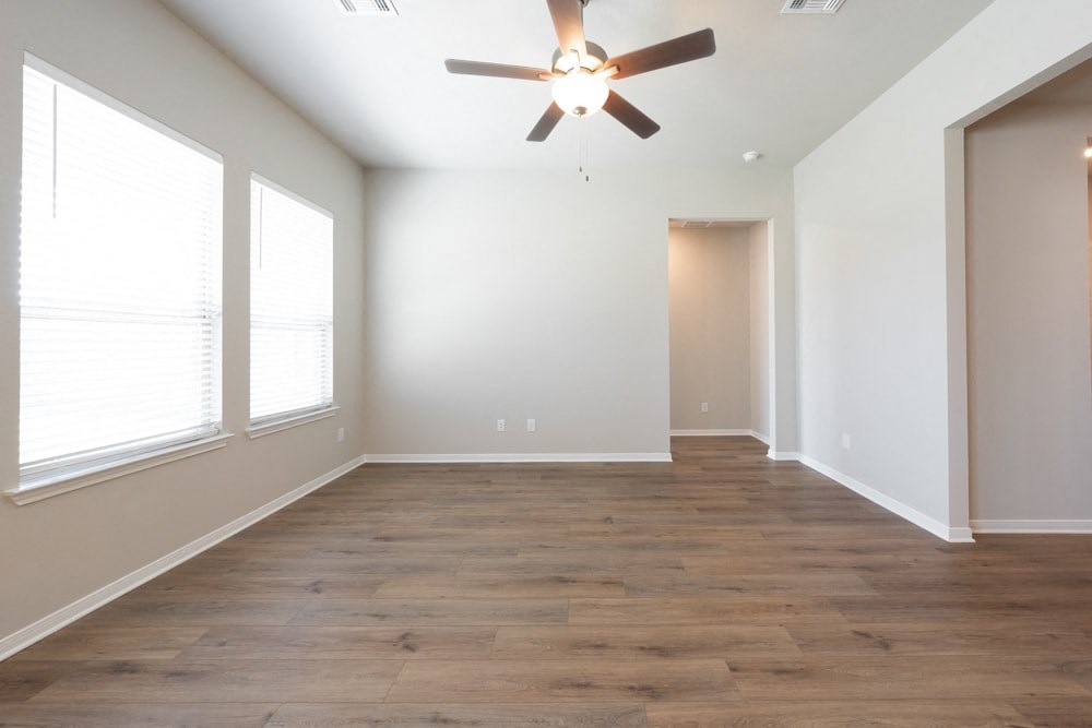 an empty living room with a ceiling fan and three windows