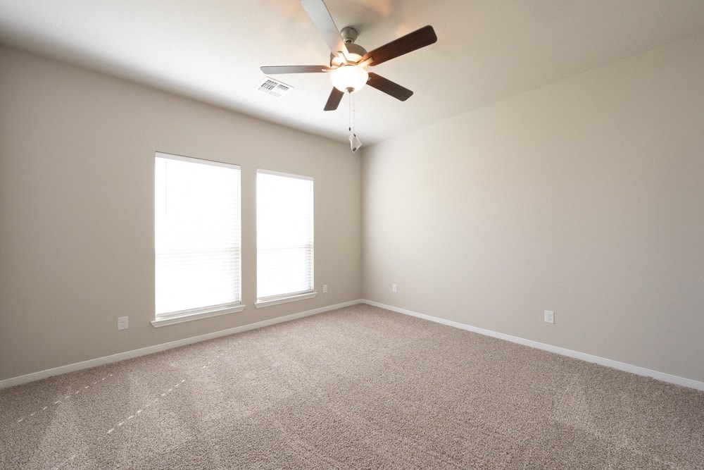 an empty living room with a ceiling fan and two windows