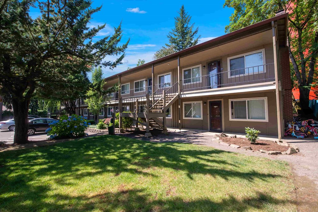 the exterior of a condominium building with a lawn and trees