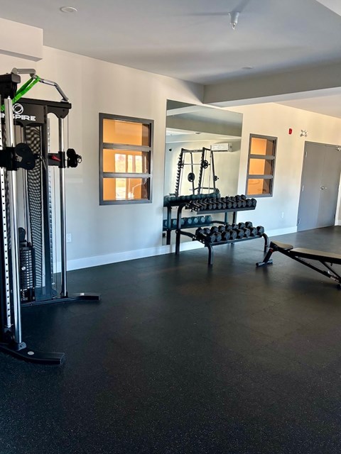 A gym with a weight machine, a bench and a rack of dumbbells.