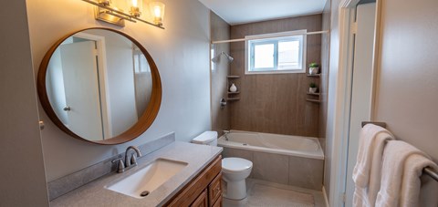 A bathroom with a round mirror, a sink, a toilet, and a bathtub.