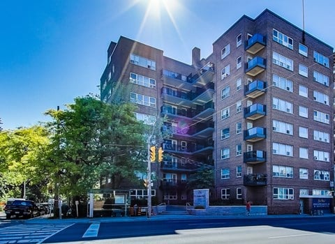 A sunny day in front of a multi-story building with a street in front.