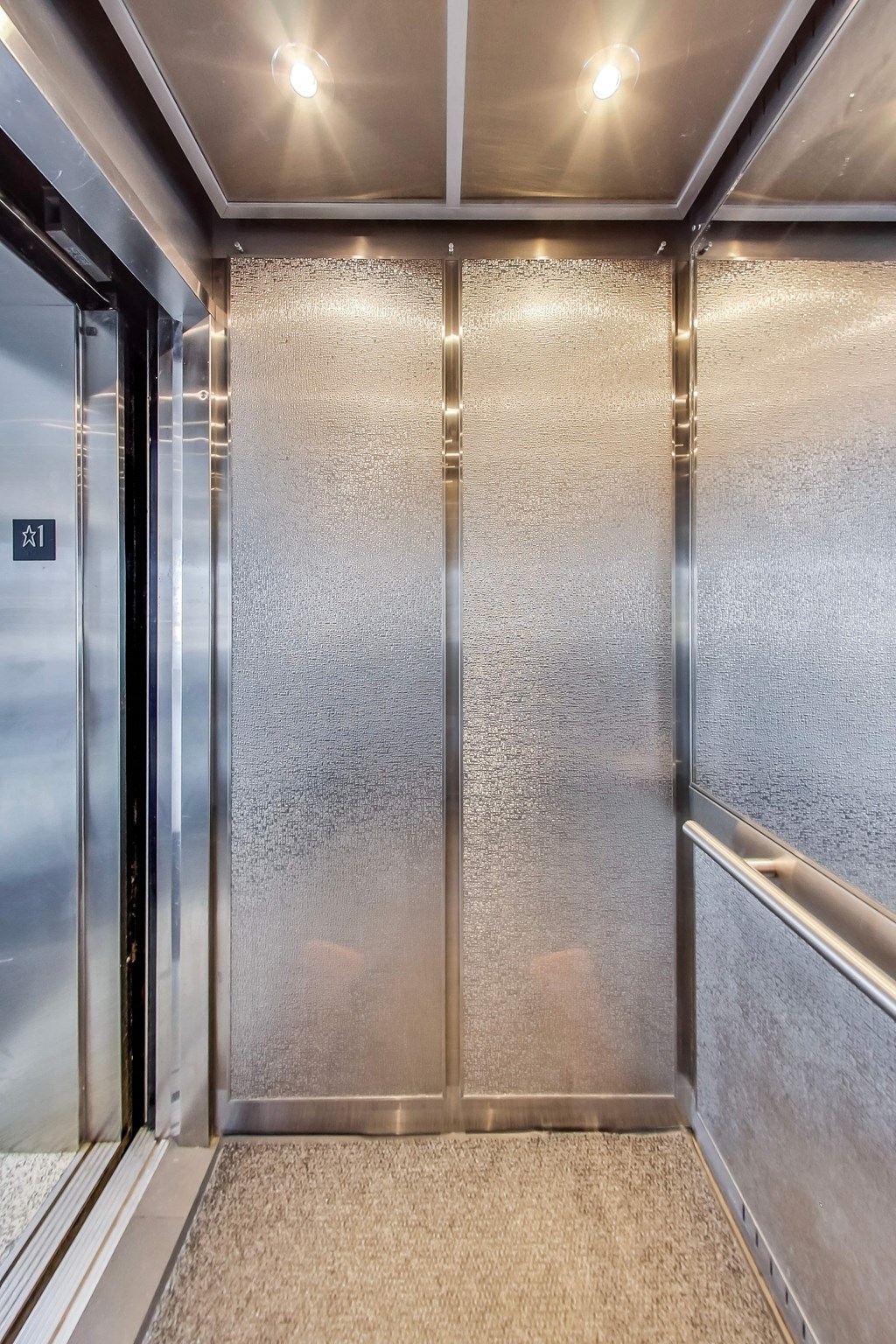 A stainless steel elevator with a glass door and a carpeted floor.