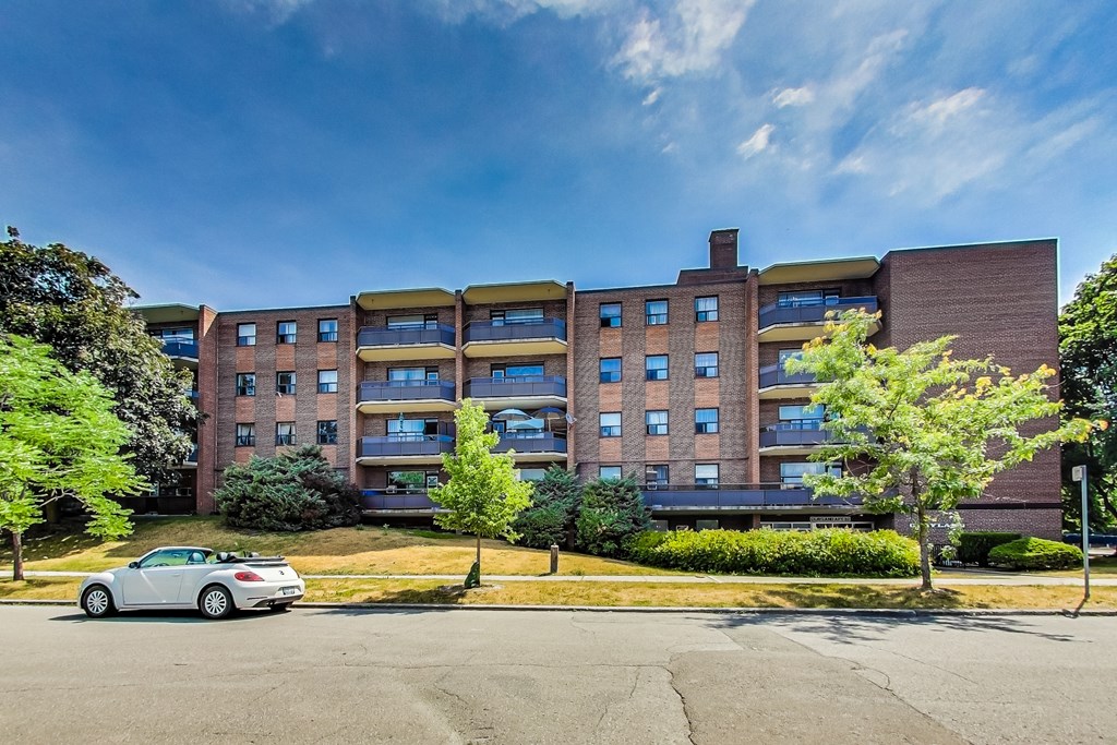 A white car is parked in front of a multi-story brick building.