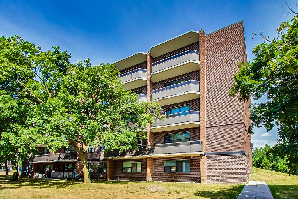 A tall apartment building with balconies and a tree in front.