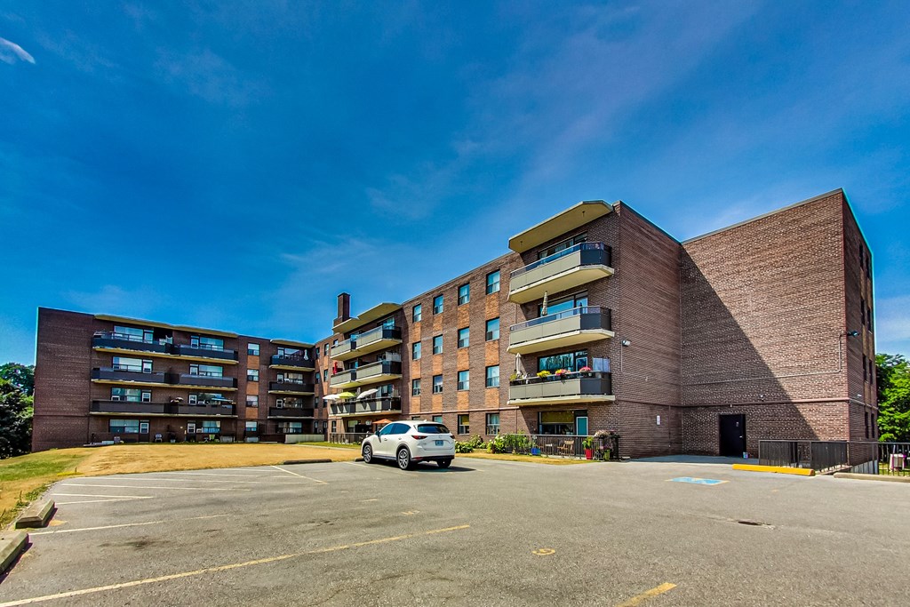 A white car is parked in a parking lot in front of a brick building.