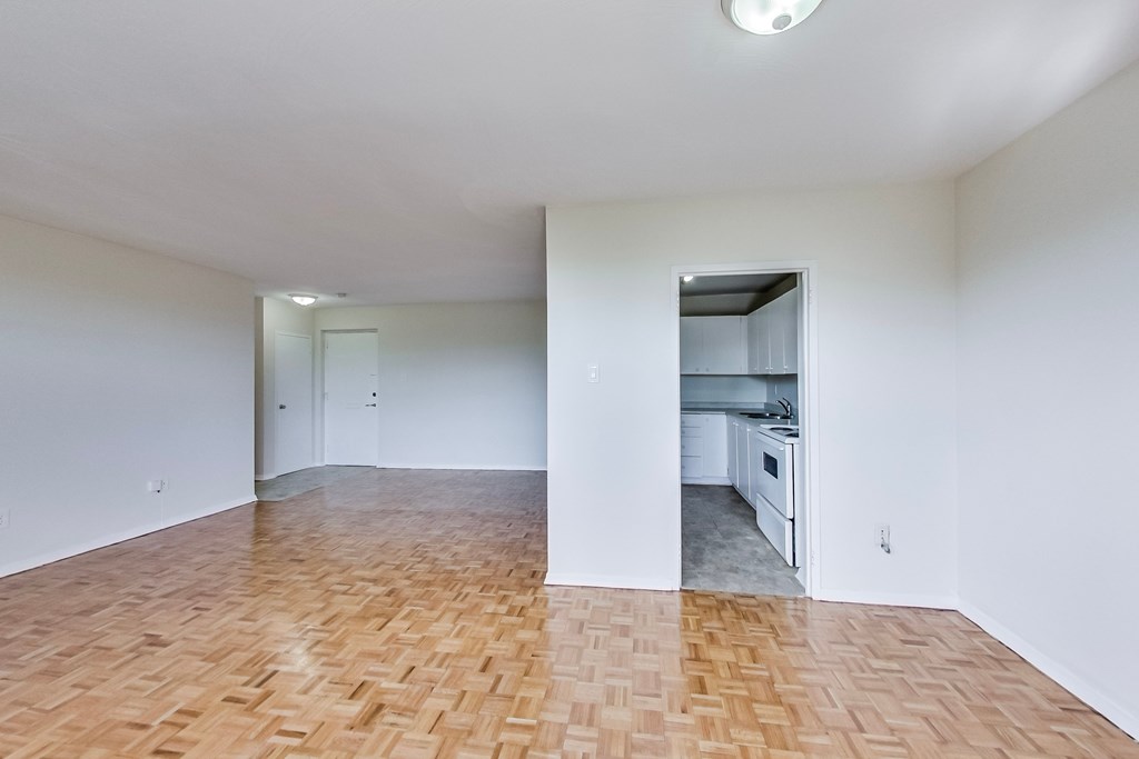 A room with a wooden floor and a kitchen in the background.