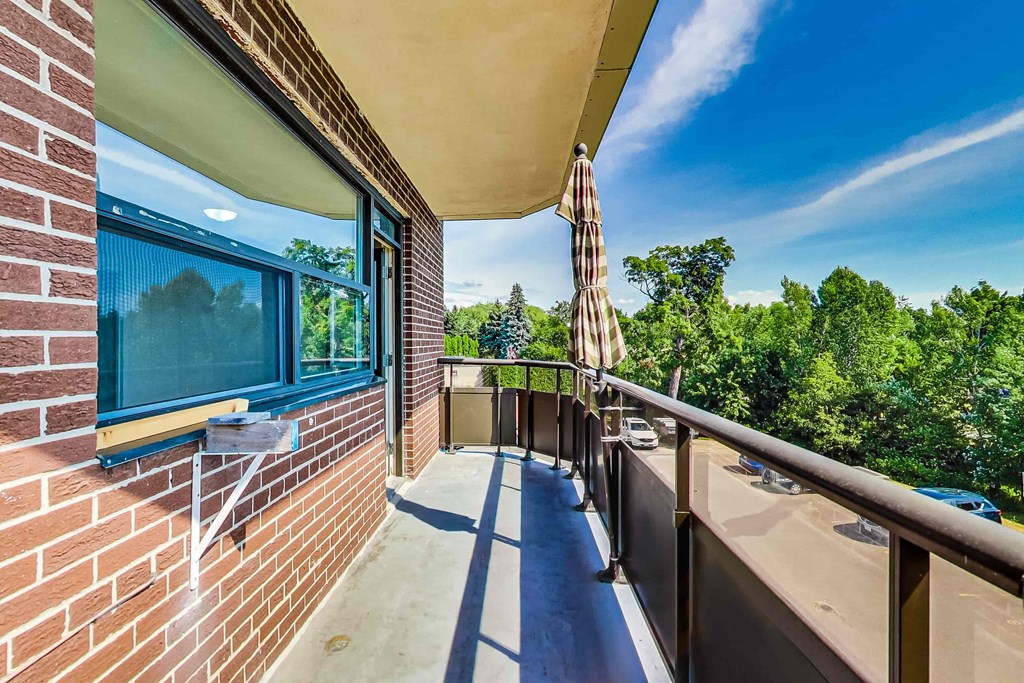 A balcony with a striped umbrella and a view of trees.