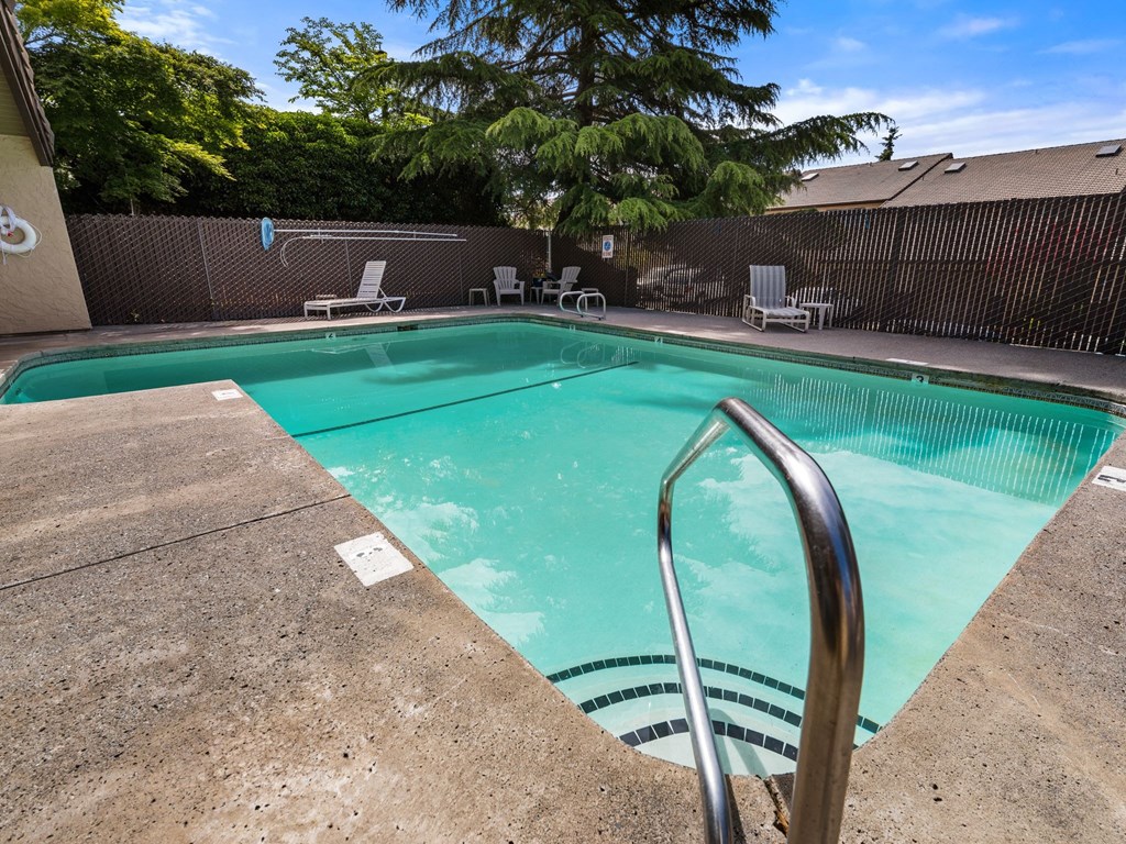 a swimming pool with a fence and chairs and a tree