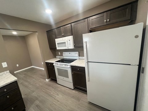A white refrigerator stands in a kitchen with a microwave, oven, and sink.