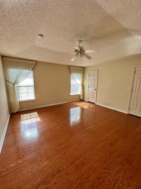 an empty living room with wood floors and a ceiling fan